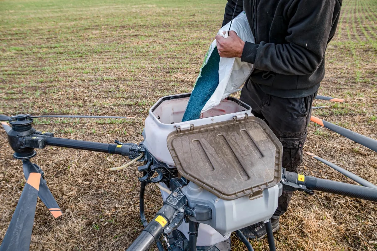 Agricultural drone spreading seeds and fertilizer over crop field